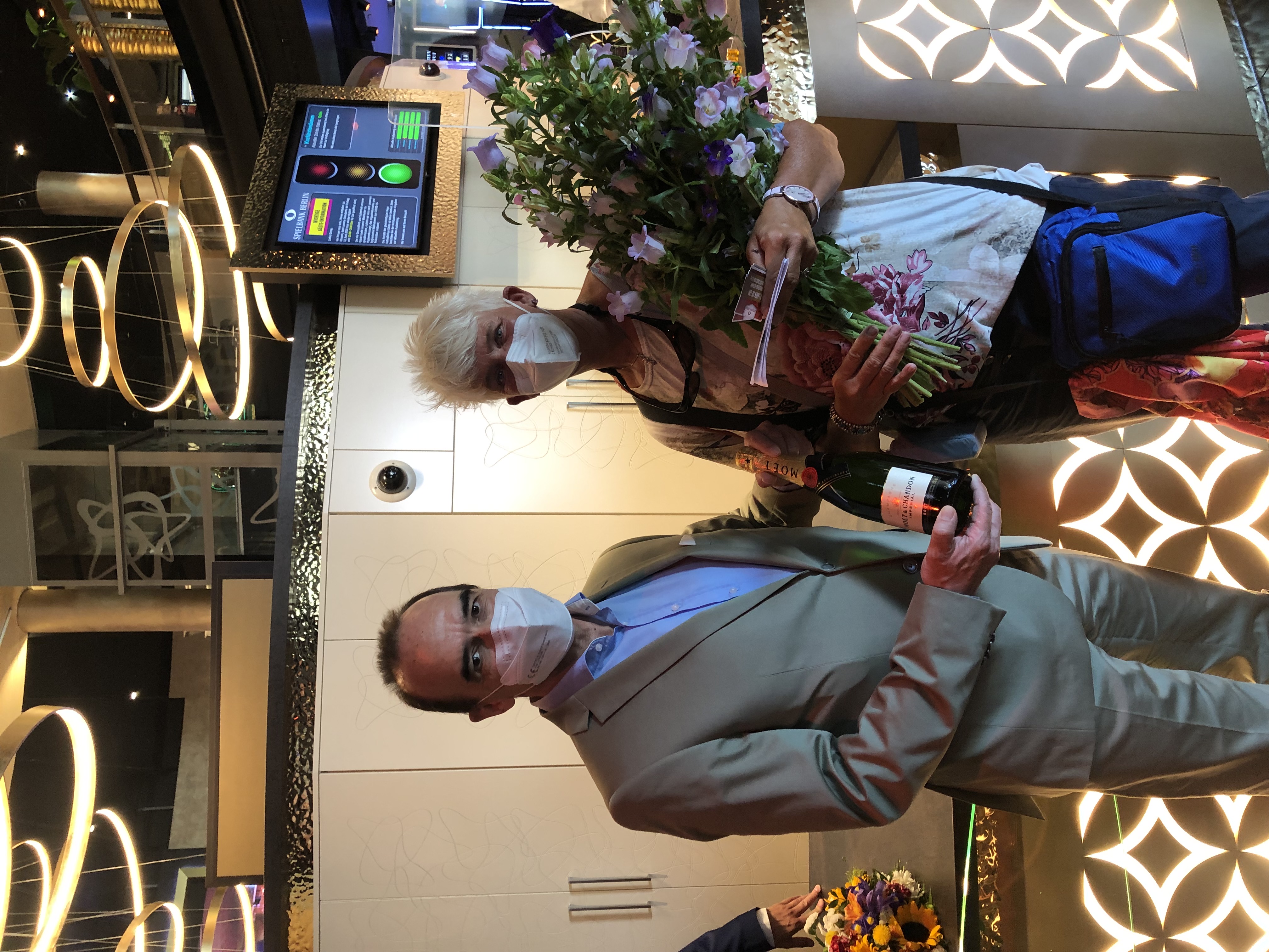 Spielbank-Chef Gerhard Wilhelm begrüßt die erste Besucherin am neuen Standort am Kurfürstendamm persönlich mit einem Blumenstrauß und einer Flasche Champagner. Foto: Spielbank Berlin